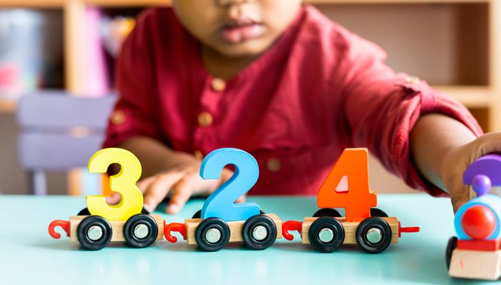 A toddler in a red shirt plays with a wooden toy train with the numbers 3,2,4 on it