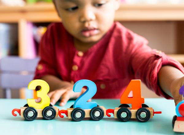 A toddler in a red shirt plays with a wooden toy train with the numbers 3,2,4 on it