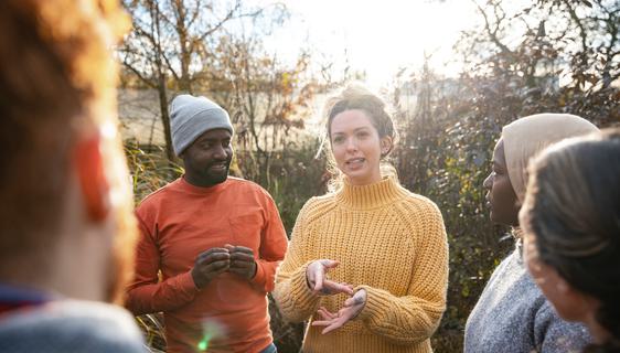 A woman in a yellow jumper is explaining something to a diverse group of volunteers