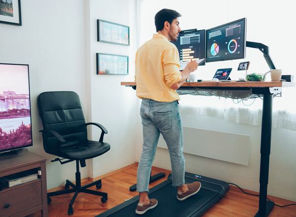 A man works from home on a standup desk whilst walking on a treadmill