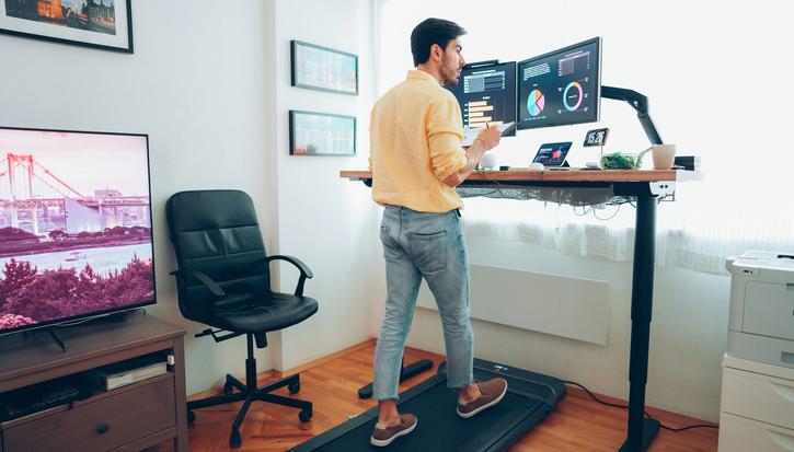 A man works from home on a standup desk whilst walking on a treadmill