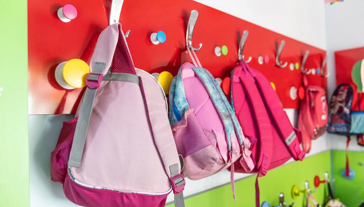 A closeup of children's rucksacks hung on hooks in a school