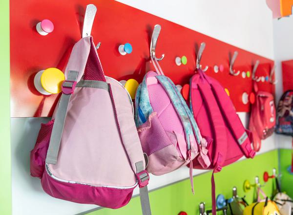 A closeup of children's rucksacks hung on hooks in a school