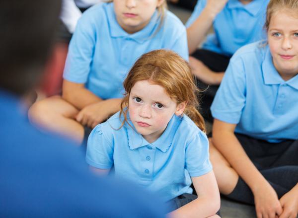 A primary school pupil sits cross-legged in a class, looking at the camera